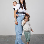 Woman stands next to young girl while carrying baby on her back in Izmi Breeze Baby Carrier