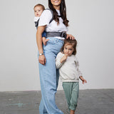 Woman stands next to young girl while carrying baby on her back in Izmi Breeze Baby Carrier