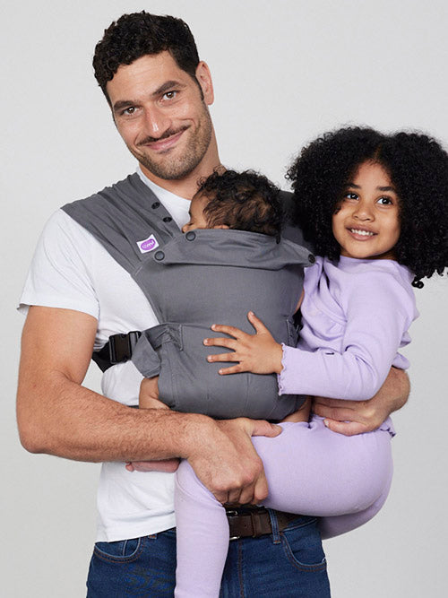 Man carries baby in Izmi Baby Carrier while holding girl on his hip