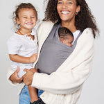 Woman carries baby facing towards her in Izmi Baby Wrap in Grey colour while holding toddler on her hip