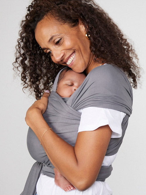 Woman carries baby facing towards her in Izmi Baby Wrap in Grey colour