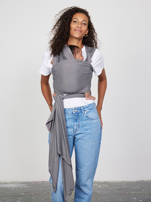 Woman carries baby facing towards her in Izmi Baby Wrap in Grey colour