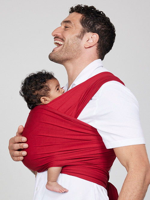 Man carries baby facing towards him in Izmi Baby Wrap in Red