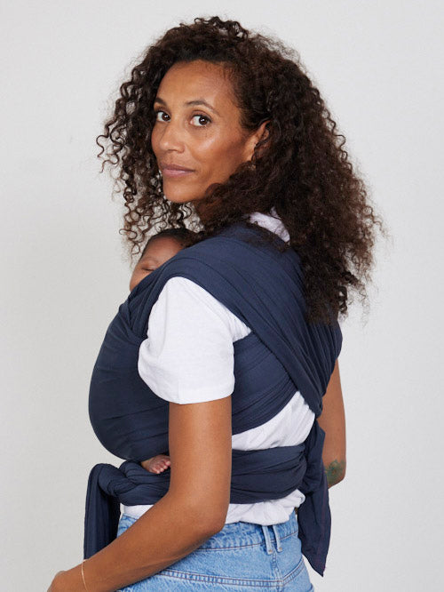 Woman carries baby facing towards her in Izmi Baby Wrap in Slate colour, back view