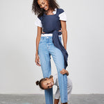 Woman carries baby facing towards her in Izmi Baby Wrap in Slate colour while toddler peeks between her knees