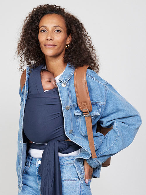 Woman carries baby facing towards her in Izmi Baby Wrap in Slate colour