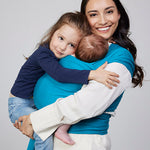 Woman carries baby facing towards her in Izmi Baby Wrap in Teal colour while also holding young girl