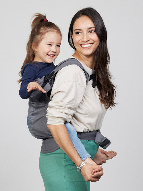 Woman carries toddler on her back in Izmi Breeze Toddler Carrier, side view