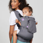 Woman carries toddler on her back in Izmi Toddler Carrier with Zip Pocket attached