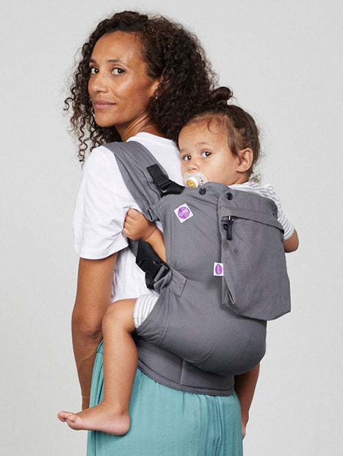 Woman carries toddler on her back in Izmi Toddler Carrier with Zip Pocket attached