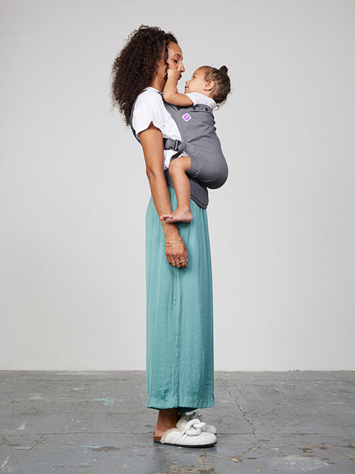 Woman carries toddler on her front in Izmi Toddler Carrier, side view